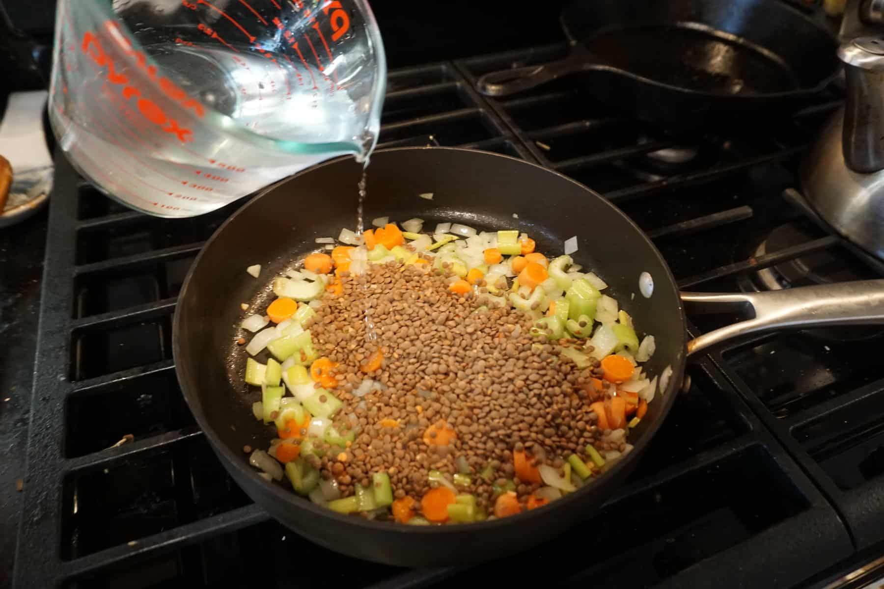 pouring water into a skillet to prepare lentils