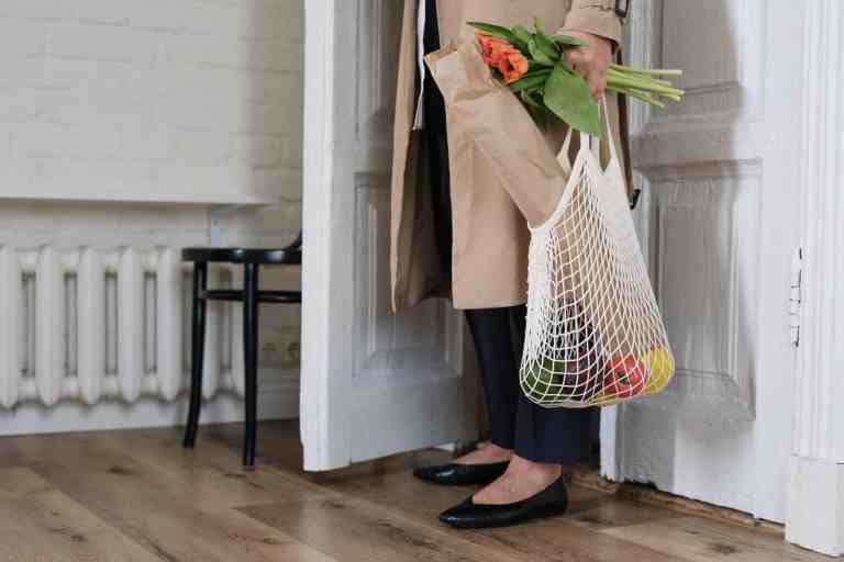 woman standing near the door holding a sustainable shopping bag and flowers