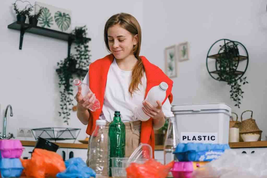 positive female sorting plastic bottles in kitchen in apartment to avoid unsustainable living