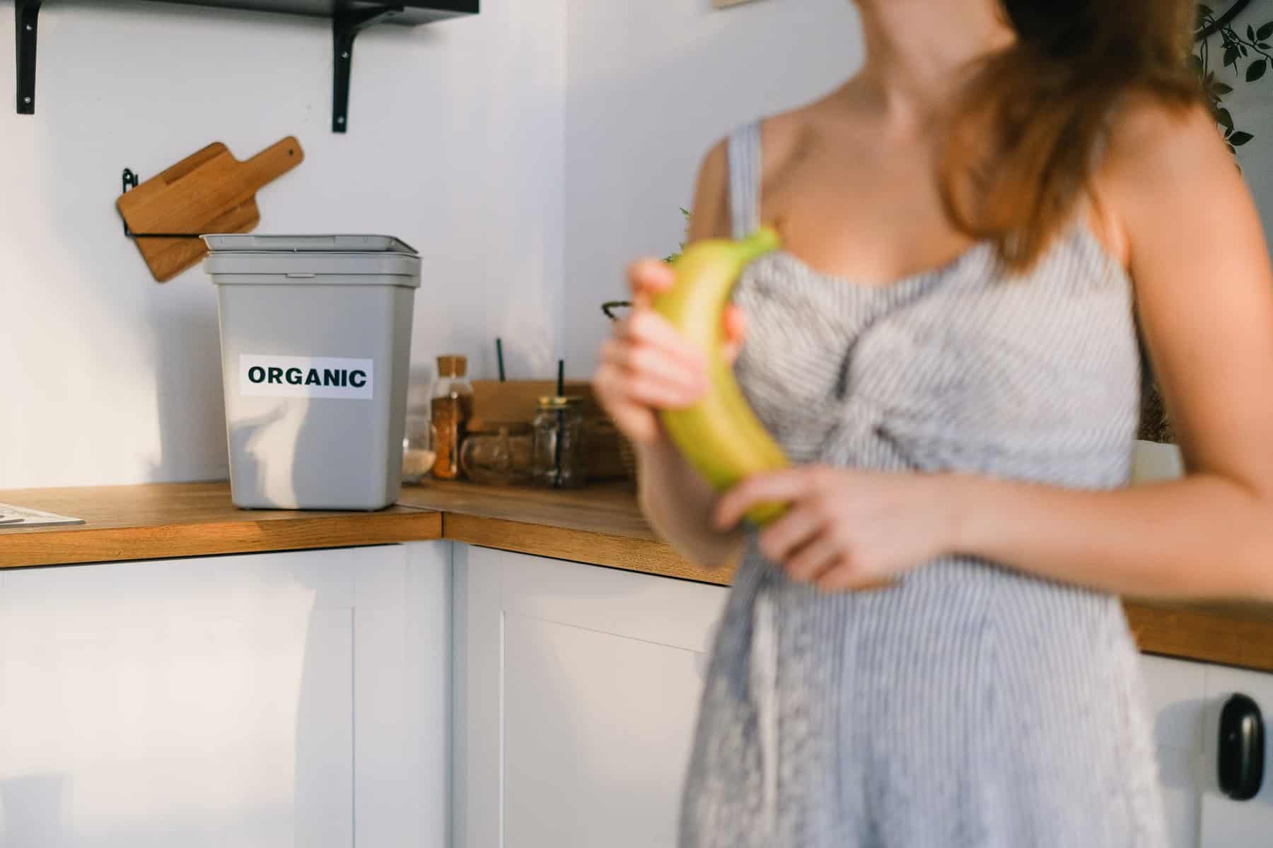 crop woman with organic banana in hands standing in kitchen