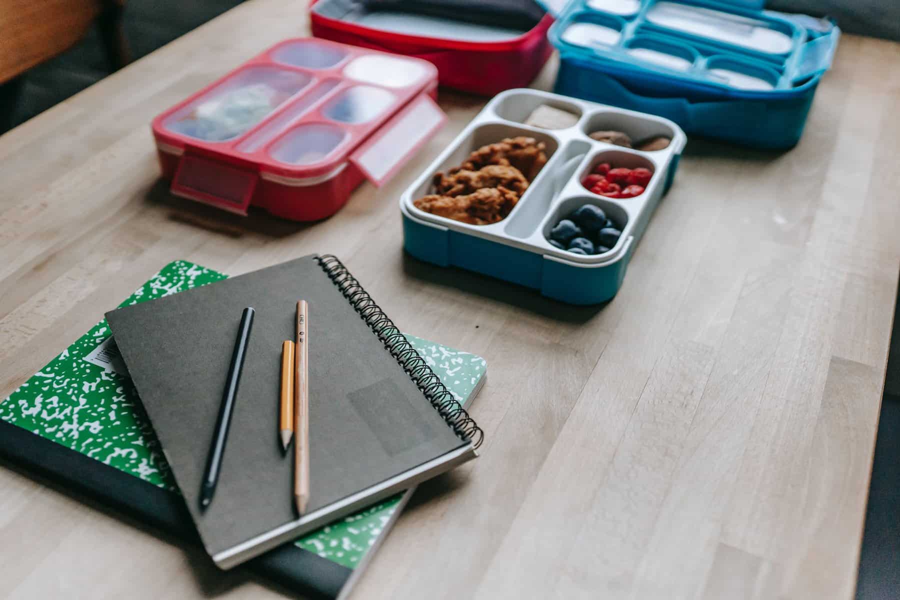 lunch boxes behind notebooks on table is an idea of breakfast on the go for the office