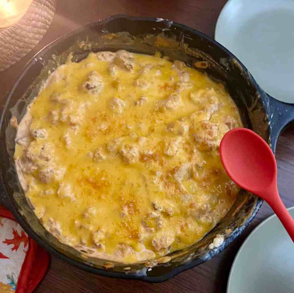buffalo cauliflower dip with red spoon in a cast iron skillet covered with cheese
