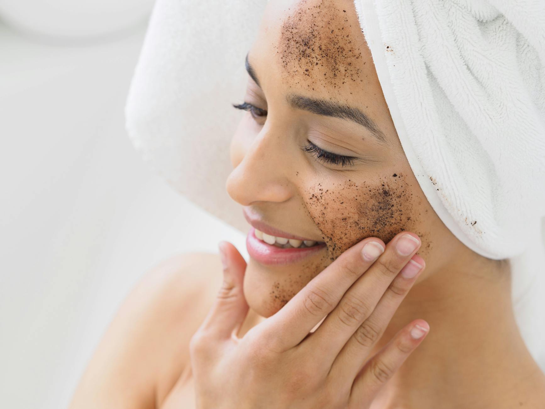 a woman putting on a face mask of used coffee grounds