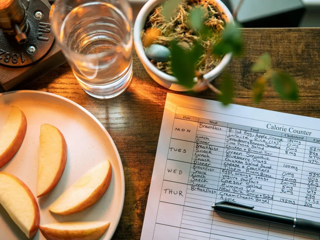 glass of water beside slices of apple and record on calorie count on brown wooden table